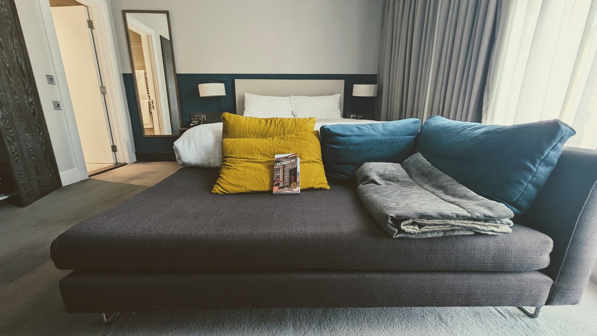 Grey sofa with yellow pillows and king bed in IHG Staybridge London Vauxhall hotel